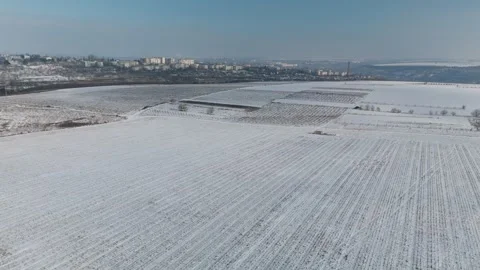 Snow-covered agricultural fields with distinct furrows and distant city skyline Vídeo Stock 332723873