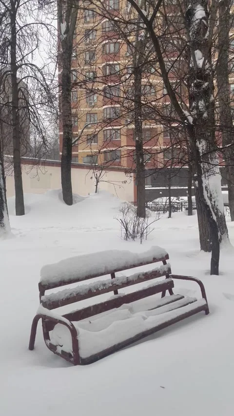 A snow-covered bench sits empty in a quiet city park. Stock Footage 326053418