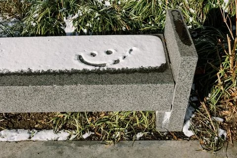 Snow-covered bench with a smiley face drawn in the snow during winter at a local Stock Photos