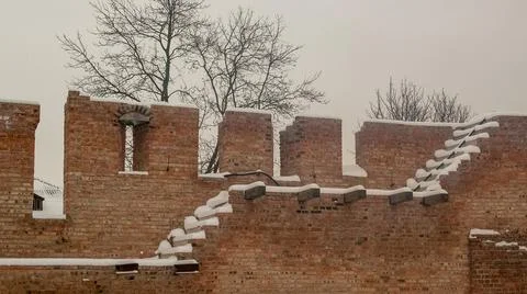Snow-Covered Brick Wall with Battlements and Bare Trees Stock Photos