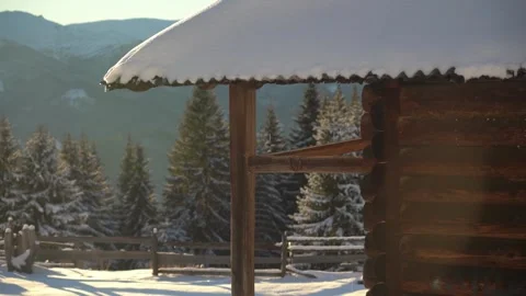 Snow-covered cabin surrounded by tall trees in a mountainous winter landscape Video stock 313482473