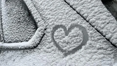 Snow-covered car window features a heart shape etched into the frost, showcasing Stock Photos