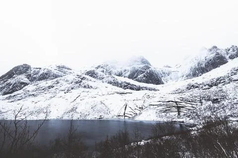 Snow-covered cliffs of Batman Wall rise over a dark Arctic lake on Lofoten,.. Photos