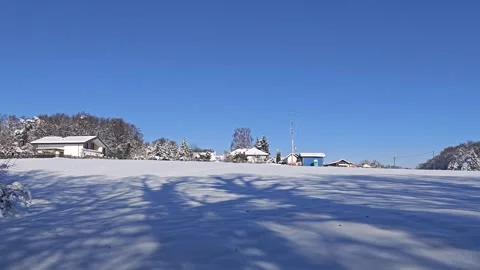 Snow Covered Field Under Clear Blue Sky With Village in Background Stock Footage 326049597