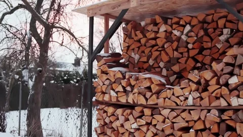 Snow-covered firewood stacked under an outdoor shed at sunset, winter home Stock Footage 327689876