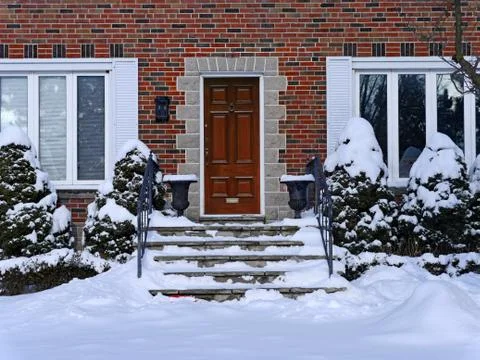 Snow covered front steps of brick house with elegant wooden door Stock Photos