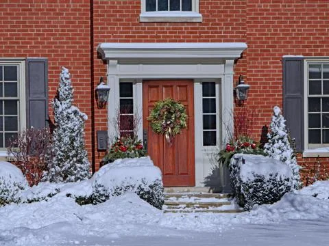 Snow covered front yard and wooden door with Christmas wreath Stock Photos