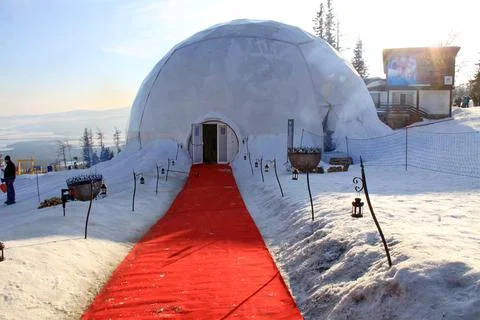 A snow-covered geodesic dome structure with a red carpet at the entrance Stock Photos