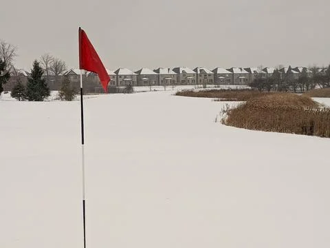 Snow Covered Golf Course with Red Flag and Suburban Houses Stock Photos