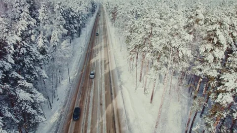 Snow-covered highway in winter with vehicles traveling through a forest 스톡 동영상 291375448