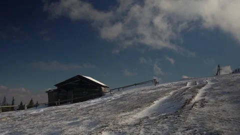 Snow-covered hillside with a rustic cabin and clear blue sky during winter Stock Footage 289401049