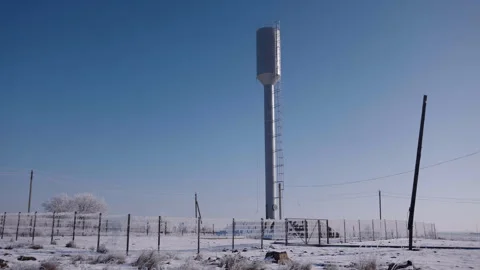 Snow-covered landscape featuring a tall water tower surrounded by a fence and Stockbeeldmateriaal 333868456
