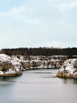 Snow covered limestone cliffs surround tranquil lake in winter landscape Stock Photos