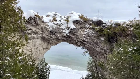 Snow covered limestone natural arch formation overlooking the frozen lake in win Stock Footage 325478158