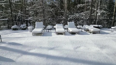 Snow covered lounge chairs next to closed shuttered swimming pool in winter Stock Footage 300886331