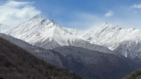 Snow covered mountain peaks stand above a broad valley beneath clouds across an Stock Footage 335076796
