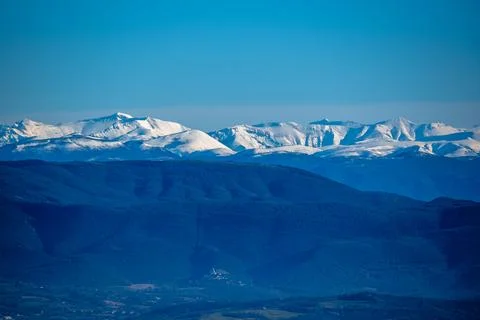 Snow covered mountain range above layered hills Stock Photos