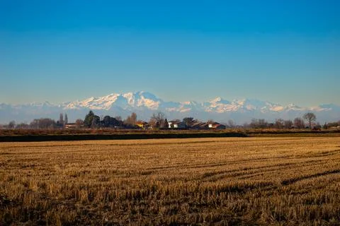 Snow-Covered Mountain Range Behind Rural Agricultural Fields and Village Hous Stock Photos