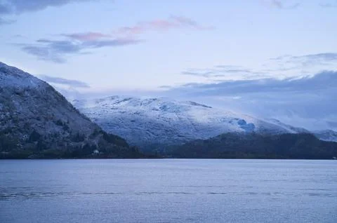 Snow-covered mountain range by a calm fjord at twilight Stock Photos
