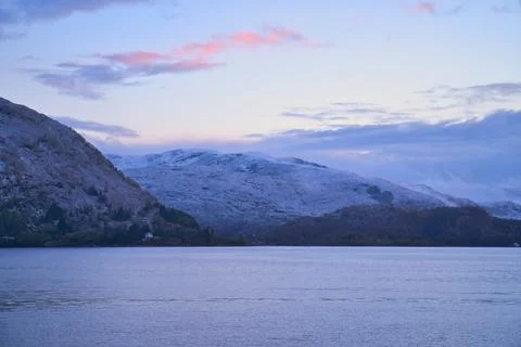 Snow-covered mountain range by a calm fjord at twilight Stock Photos