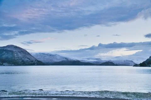 Snow-covered mountain range by a calm fjord at twilight Stock Photos