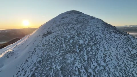Snow-covered mountain rises above dense evergreen forest during sunrise in a Stock Footage 319477884