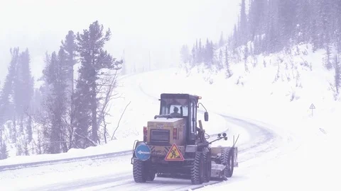 Snow-covered mountain road in winter. The machine cleans the service road. Video stock 72893522