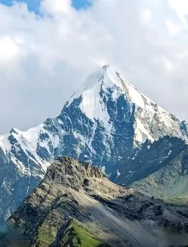 Snow covered mountain summit surrounded by clouds and rocky ridge terrain Stock Photos