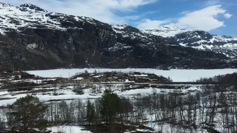 Snow-Covered Mountains and Sparse Trees in Norwegian Valley Under Blue Spring Stock Footage 340877359