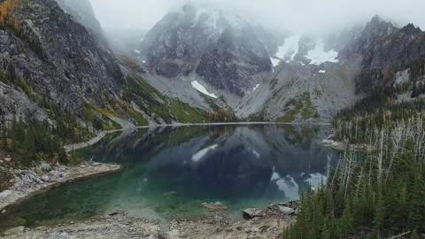 Snow covered mountains reflect in tranquil lake surrounded by lush forest Stock Footage 312718964
