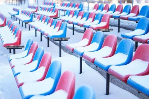 Snow-covered multi-colored seats in the stadium in winter. Snowfall interfere Foto stock