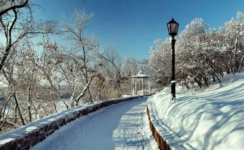 Snow-covered path in a winter park with a gazebo Stock Photos
