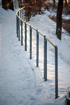 A snow-covered pedestrian path with segmented metal railings. The railings .. Stockfoto's
