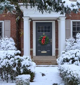 Snow covered pine tree and shrubbery in front of traditional brick house Foto stock
