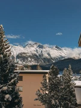 Snow covered pine trees framing a chalet with majestic mountain peaks in the Stock Photos