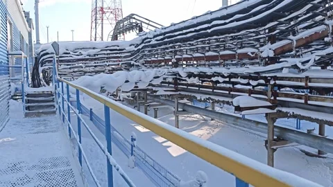 Snow covered pipe racks frame industrial walkway beside blue railings. Winter 스톡 동영상 347037132