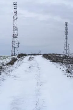 Snow-covered road leads to communication towers in a rural area during winter Stock Photos