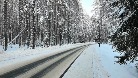 Snow-covered road through a forest in winter showing trees and a clear sky Stock Footage 327104081