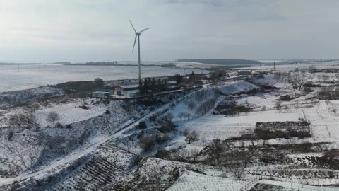 Snow-covered rural landscape with wind turbine, farm buildings, and fields Vídeo Stock 332724027