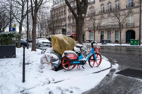 Snow-covered shared bicycle and garbage bags on Avenue George V in Paris, France Stock Photos