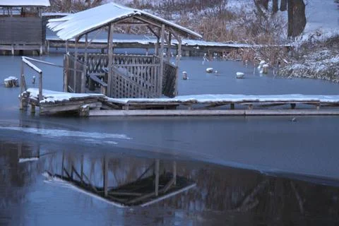 Snow-covered wooden gazebo reflected in a frozen lake. Stock Photos