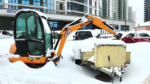 Snow covers a construction site with a digger and trailer parked in the lot on a Stock Footage 328488517