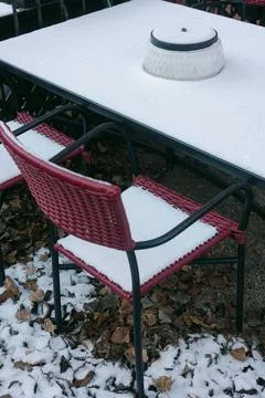Snow covers empty chairs at a table in a quiet outdoor cafe setting during Stock Photos