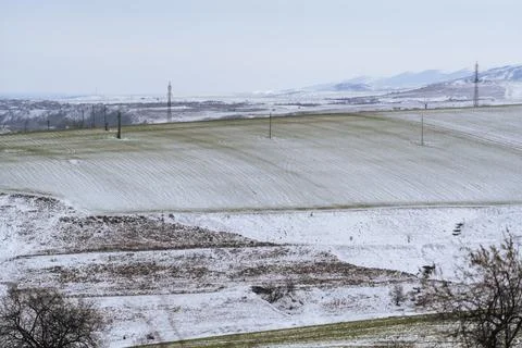 Snow covers fields in a rural area during winter with hills in the background Stock Photos