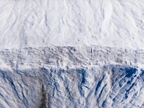 Snow covers a surface with patterns of white and gray in a winter landscape.. Photos