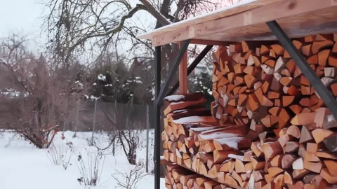 Snow-dusted firewood stacked under a simple shed in a rural backyard, showing Stock Footage 327889387