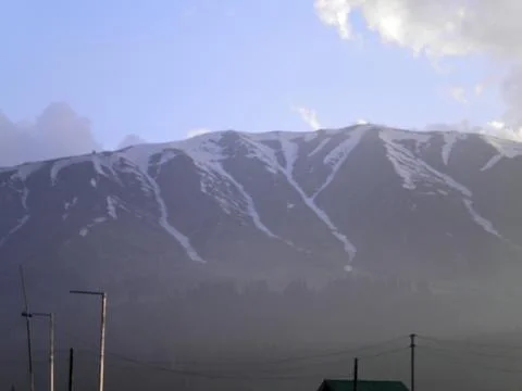 Snow-dusted mountain range under a clear blue sky with a hint of clouds Stock Photos