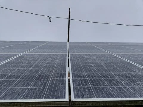 Snow-dusted solar panels under overcast sky for renewable energy solutions Stock Photos