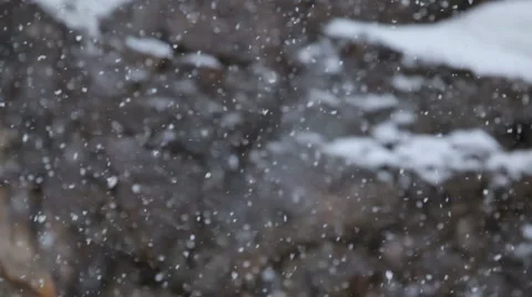 Snow falling as camera tilts down with rock cliff in background Stock Footage 1084899