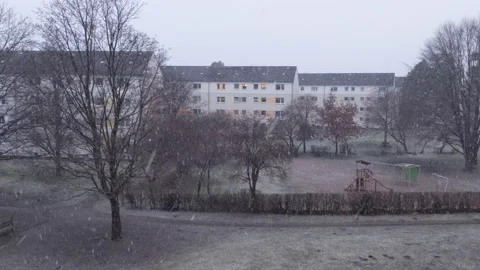 Snow falling in city park surrounded by apartment buildings, establishing shot Stock Footage 238901356